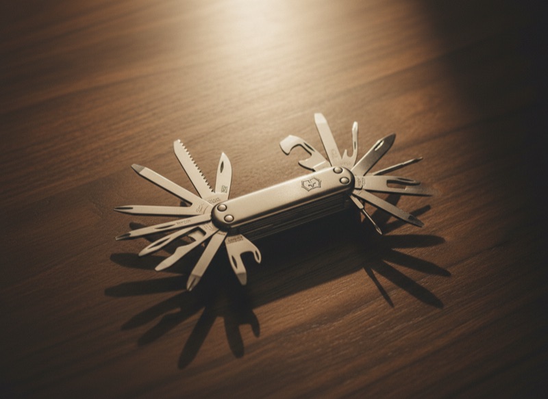 An opened vintage multi-tool with its implements fanned out symmetrically on dark walnut, lit from one side.
